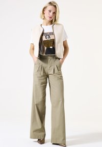 Chaleco de forro polar beige con cremallera frontal, camiseta gráfica blanca con un diseño de estampado de leopardo y pantalones de khaki holgados con pinzas.
