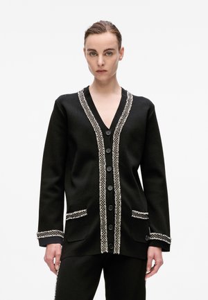 Schwarze Strickjacke mit V-Ausschnitt, verziert mit einem weißen strukturierten Saum, ausgestattet mit sechs Knöpfen und zwei Vordertaschen. Glattes Material mit einer taillierten Passform.