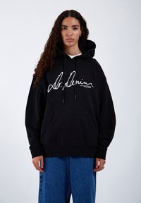 Black hoodie with large, white signature logo on the front. Features a drawstring hood, kangaroo pocket, and ribbed cuffs. Soft texture.
