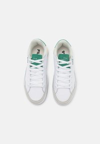 Sneakers bianchi con tomaia in pelle liscia, dettagli verdi sulla linguetta e suola in gomma grigia texture. I lacci sono piatti e intrecciati.