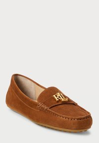 Bruine suede instappers met een gestikt ontwerp en een gouden logo-accent aan de voorkant. Getextureerde zool met kleine uitsteeksels voor grip.
