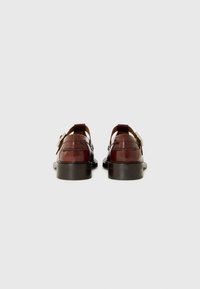 Braune Lederschuhe mit glänzender Oberfläche, seitlichen Ausschnitten, einem Riemen mit Schnalle und einer stabilen schwarzen Sohle.