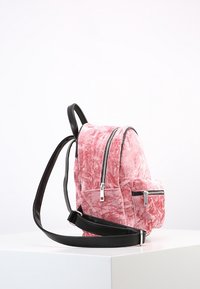 Mochila de terciopelo rosa con detalles brillantes en negro, superficie texturizada, doble compartimento con cremallera y correas de hombro ajustables.