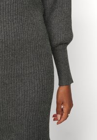 Grå ribbad trikåklänning med åtsittande silhuett, långa ballongärmar och en texturerad yta, med en slät finish nära handleden.