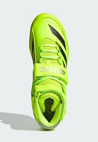 Chaussure de sport néon vert brillant avec des accents noirs, tige en maille, bout fermé et sangle de cheville sécurisée pour la stabilité. Détail de surface texturée.