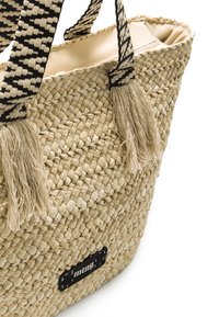 Bolso de paja tejido con asas de patrón en blanco y negro y dos borlas. Presenta una forma rectangular y una etiqueta de marca negra.