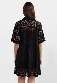 Rochie neagră din dantelă, cu mâneci scurte, croială lejeră și un design transparent, prezentând un model floral și o lungime deasupra genunchiului.