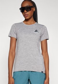 Γκρι κοντομάνικο μπλουζάκι από μαλακό, υφασμάτινο υλικό, με γραφικό βουνό και λογότυπο στο αριστερό στήθος. Φοριέται με μπλε παντελόνι για εξωτερικές δραστηριότητες.