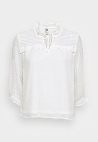 White blouse made of textured fabric with a polka dot pattern, featuring a ruffled neckline, tie closures, and three-quarter sleeves.