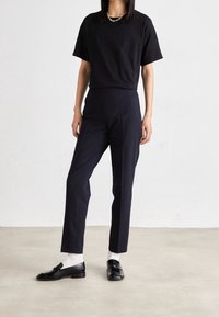 Black short-sleeve t-shirt paired with tailored dark navy trousers and black loafers over white socks. Simple, modern design with clean lines.