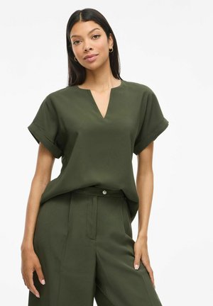 Blusa verde oliva con escote en V, mangas cortas enrolladas y un corte holgado, combinada con pantalones de tiro alto a juego. Textura de tela suave.