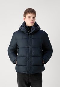 Veste rembourrée navy avec un design matelassé, boutons à l'avant et capuche amovible. Tissu texturé avec poches latérales et col montant.