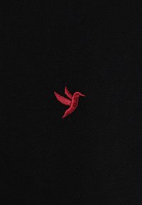 Schwarzer Stoff mit einem roten gestickten Kolibri-Muster, das mit detaillierten Stichen und einer glatten Textur versehen ist.