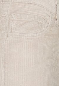 Lichtbeige corduroy stof met ribbelstructuur, voorzien van een achterzak en subtiele stikdetails.