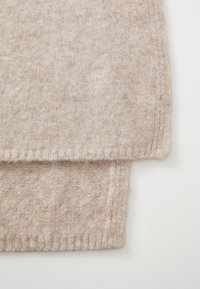 Beżowy sweter dzianinowy z teksturowanym wzorem, z prążkowanymi mankietami i dołem, miękkiego materiału oraz widocznymi szwami wzdłuż krawędzi.