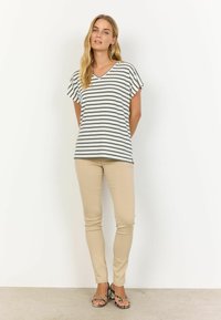 Stribet v-hals top i hvid og mørkegrøn med korte, lette ærmer; parret med beige tætsiddende bukser og mønstrede sandaler.