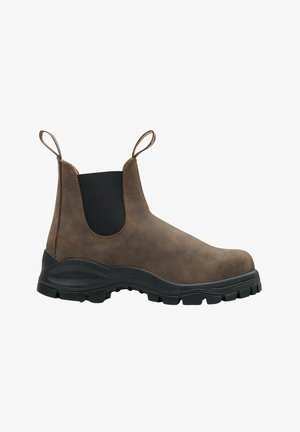 Brązowy skórzany but za kostkę z elastycznymi panelami bocznymi, uchwytami do zakładania oraz grubą czarną gumową podeszwą z teksturowanym wzorem.