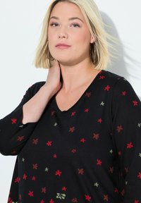 Zwarte top met een V-hals, driekwart mouwen en bloemenpatronen in rood en groen. De stof lijkt zacht en heeft een iets ontspannen pasvorm.