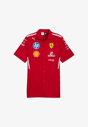 Sarkans īsajām piedurknēm pogājamais krekls, izgatavots no auduma ar baltām akcentiem. Iekļauj vairāku logo, tostarp Ferrari, HP un Shell.
