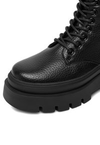 Czarne skórzane botki za kostkę o fakturowanej powierzchni, okrągłym nosku oraz grubym czarnym gumowym podbiciu. Posiada okrągłe oczka i szczegóły związane z sznurowaniem.