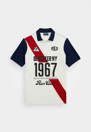 Polo em branco, azul-marinho e vermelho. Apresenta mangas curtas, colarinho, faixa diagonal vermelha, logótipos e detalhes em texto em negrito.