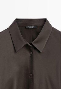 Chemise en satin marron foncé avec col pointu et deux boutons visibles, affichant l'étiquette de la marque Massimo Dutti à l'intérieur du col.