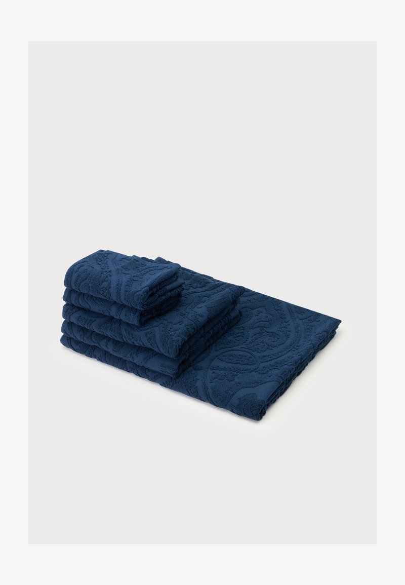 Pile de quatre serviettes bleu marine texturées de tailles variées sur un fond clair, affichant des motifs en relief complexes.