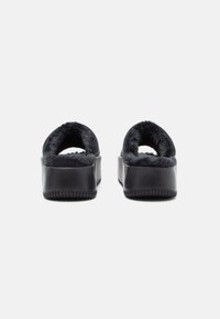 Zapatillas de plataforma negras con un interior suave forrado de piel y diseño de talón abierto. La suela tiene textura para ofrecer agarre y estabilidad.