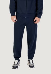 Dunkelblaue Jogginghosen aus einem weichen Material, mit einer lockeren Passform, elastischem Bund und seitlichen Taschen. Mit einem Logo-Patch akzentuiert.