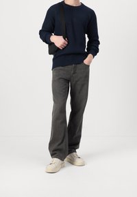 Marinblå ribbad stickad tröja med långa ärmar, grå vida jeans och krämfärgade sneakers. Modellen bär en liten svart väska.