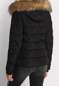 Doudoune noire avec des coutures horizontales, une capuche et un col en fausse fourrure marron clair. Comprend des poignets côtelés et des poches latérales.