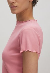 Roze ribbed t-shirt met een hoge halslijn en geschulpte korte mouwen. De stof lijkt soepel en iets rekbaar.