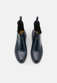 Botas de goma azul marino hasta el tobillo con un acabado brillante, paneles laterales elásticos y tiradores para facilitar su uso. Suelas planas con interiores texturizados.