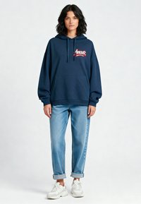 Felpa blu navy con ricamo "Amour", tasca a marsupio e cappuccio con coulisse. Abbinata a jeans azzurri risvoltati e sneakers bianche.