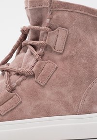 Sneaker high-top in suede rosa con superficie testurizzata, lacci piatti e occhielli discreti; presenta suola in gomma bianca e imbottitura morbida.