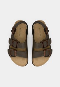 Brown sandals with three adjustable straps, copper-tone buckles, and a textured footbed, featuring a minimalist design.