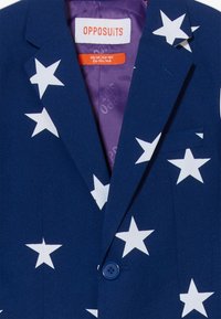 Tumesin, millel on suured valged tähek илумused, kangas on sile, ühe nupuga kinnitamine ja rinnatasku. Sees on lilla vooder.