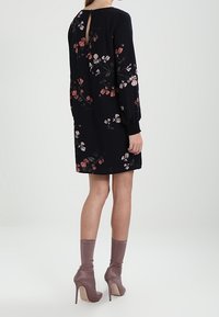 Vestido negro con estampado floral y mangas largas, que presenta flores en tonos rosa y blanco. Detalle en forma de ojal en la espalda y silueta relajada. Combinado con tacones de un suave color rosa.