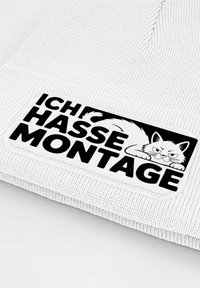 White beanie with ribbed texture, featuring a black patch displaying the text "ICH HASSE MONTAGE" and an illustrated cat design.