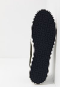 Sko med en texturerad marinblå gummisula som har ett geometriskt mönster. Sidan visar en mjuk, olivgrön tygöverdel med vita detaljer.