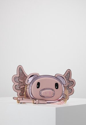 Růžová crossbody taška ve tvaru prasečího obličeje s třpytivými křídly a černýma oválnýma očima, ležící na bílém povrchu proti šedému pozadí.