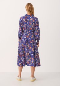 Sukienka w kwiatowy wzór w niebieskim kolorze z czerwonymi i pomarańczowymi akcentami, długie rękawy, kołnierzyk oraz spódnica do kolan. Wykonana z lekkiego materiału.