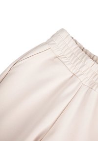 Jasnobeżowe spodnie z szerokim elastycznym paskiem w talii i bocznymi kieszeniami, wykonane z gładkiego, lekko błyszczącego materiału i o dopasowanym kroju.