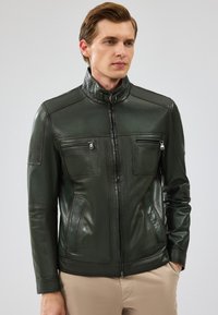 Giacca in pelle verde con colletto alto, chiusura frontale con zip, due taschini sul petto e tasche laterali con chiusura a zip. Texture liscia.