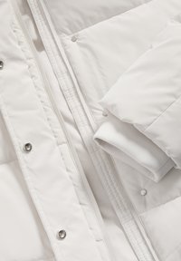 Witte pufferjack met een quilted ontwerp, soepele textuur, subtiele glans, ritsluiting en drukknoopjes aan de voorkant.