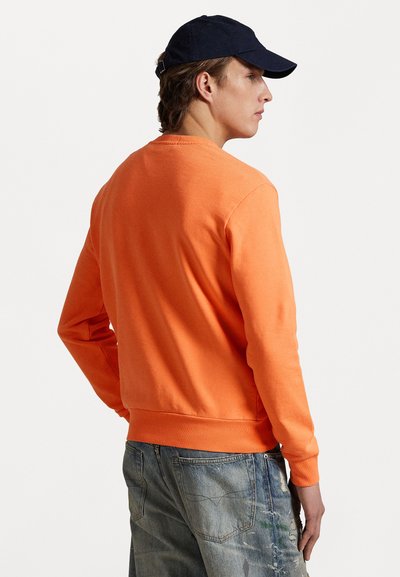 Orange sweatshirt with a crew neckline and ribbed cuffs. Paired with distressed blue denim jeans, featuring a relaxed fit and subtle textures.