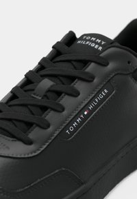 Sort lædersneaker med tekstureret overflade, flade snørebånd og et mærket label. Har et glat design og minimalistiske detaljer.