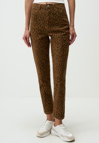 Pantalon marron à imprimé léopard avec taille haute, cinq poches et coupe droite, associé à des baskets blanches.