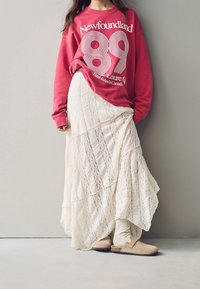 Felpa rossa con testo bianco, gonna maxi bianca a strati in tessuto testurizzato e scarpe beige slip-on con cinturino.