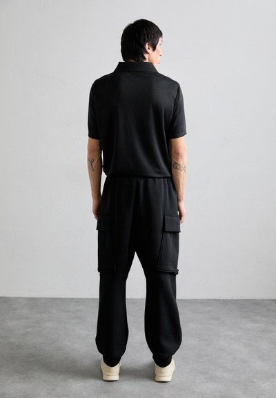 Black polo shirt with short sleeves, paired with black joggers featuring cargo pockets. Smooth texture, relaxed fit, and elastic waistband.